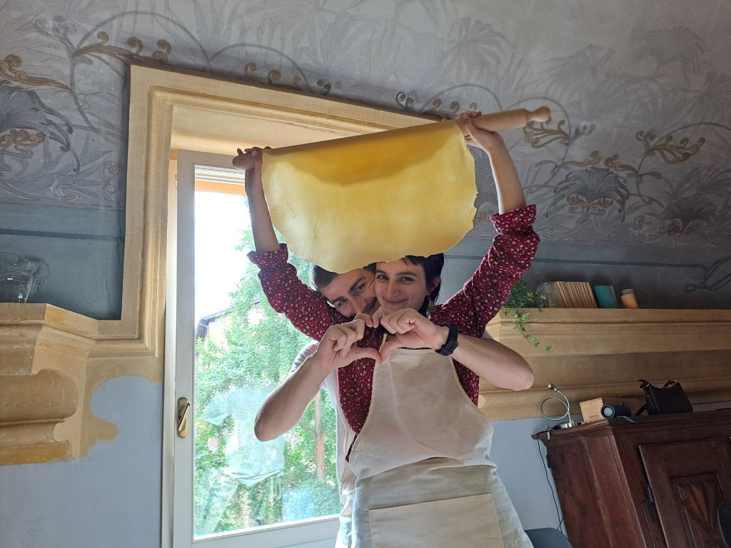 Una coppia si diverte sollevando insieme la sfoglia sottile tirata a mano durante l'esperienza Amore e Farina.