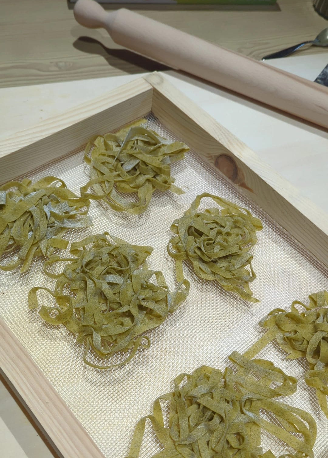 Nidi di tagliatelle verdi all'ortica appena tagliate ed essiccate su telaio di legno con mattarello.