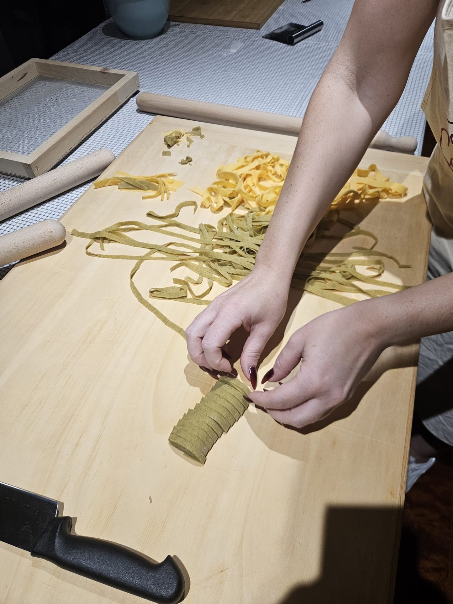 Primo piano delle mani che preparano tagliatelle bicolore gialle e verdi su un tagliere di legno tradizionale.