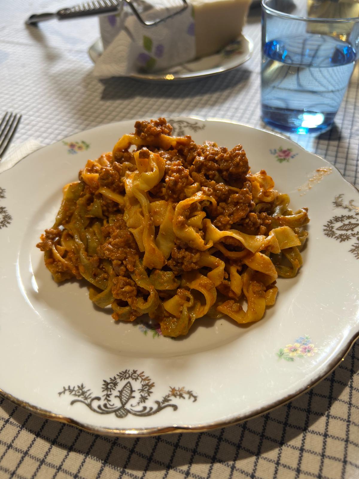 Piatto di tagliatelle fresche paglia e fieno condite con ragù bolognese tradizionale su tavola apparecchiata.